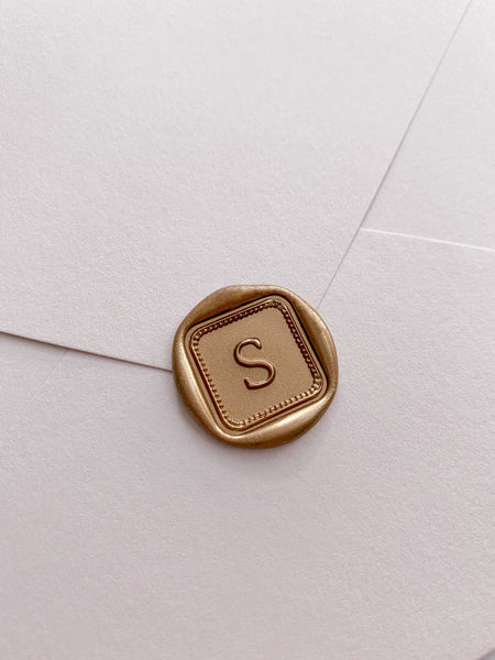 Single initial with border design mini square wax seal in gold on beige envelope