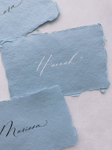 handmade paper place cards in sky color hand lettered in modern calligraphy in white ink and black ink