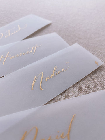 slim vellum place cards in hand lettered calligraphy in gold ink_side angle