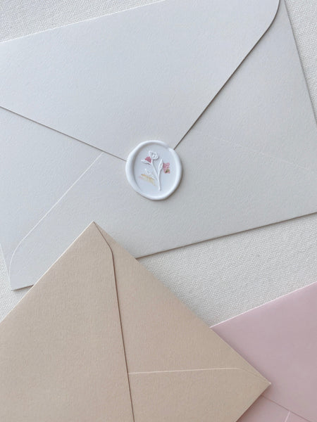 a white oval wax seal sticker with blush color dried petals on paper envelope